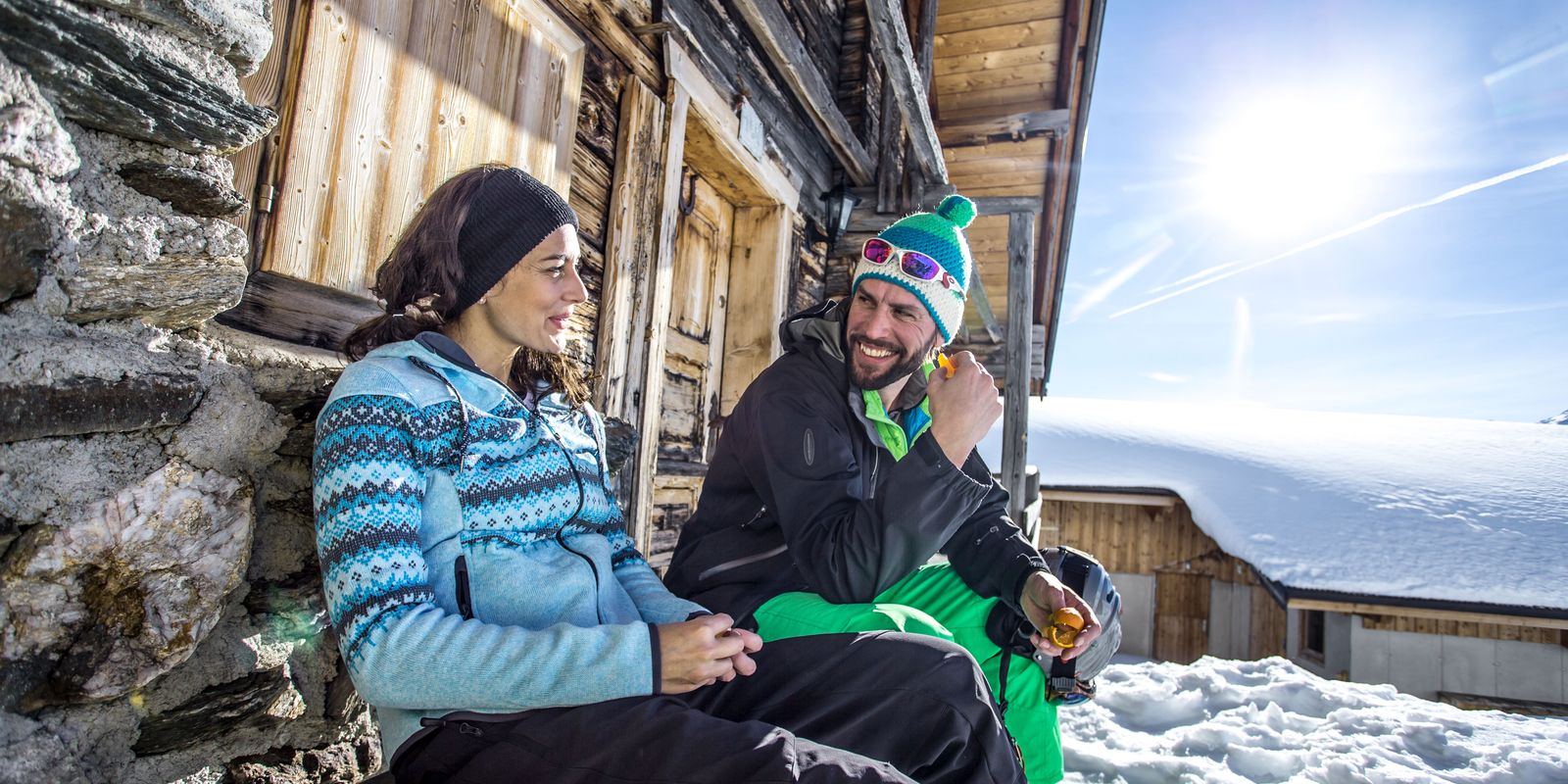 Paar beim Sonne tanken an einer Berghütte im verschneiten Skigebiet